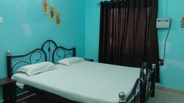 A bedroom with a bed, a nightstand, a window with curtains, an air conditioning unit, and wall decorations. - Janardan Homestay Lucknow (Lucknow)
