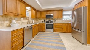 A modern kitchen with wooden cabinets, stainless steel appliances, and a striped rug.