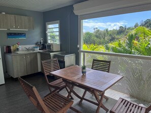 A kitchen with a microwave, sink, and cabinets, a dining area with wooden furniture, and a balcony with a view of greenery. - Villas smoothie Sycaro (Le François)