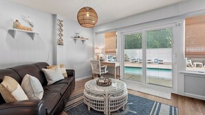 A living room with a leather couch, a round wicker coffee table, and a large sliding glass door leading to a pool area. - Hidden Gem: Private Pool | Hot Tub | Tiki Bar (Corolla)