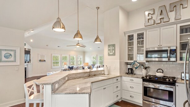 A modern kitchen with white cabinets, a large island, stainless steel appliances, pendant lighting, and a ceiling fan. - Hidden Gem: Private Pool | Hot Tub | Tiki Bar (Corolla)