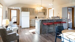 Une cuisine moderne avec des meubles en bois, un îlot central surmonté d’un auvent rouge, et un coin repas avec une table ronde et des chaises.