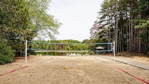 Un terrain de beach-volley sablonneux, avec un filet, entouré d’arbres et bordé par un lac.