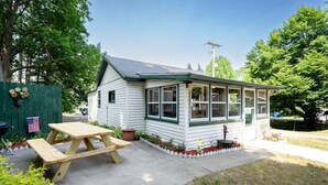 Ett litet hus i ett våningsplan med en inglasad veranda, ett picknickbord och en liten trädgårdsyta.