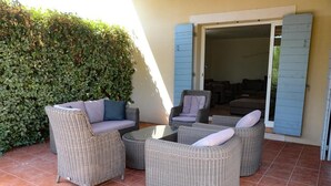 A patio area with wicker furniture, a glass table, and a view of an interior space through an open door. - Quiet family friendly vacation home for 6 to 10 pers. (Cabrieres d' Avignon)