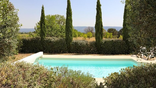 A swimming pool surrounded by tall cypress trees and dense shrubbery, with a clear view of the landscape in the background. - Quiet family friendly vacation home for 6 to 10 pers. (Cabrieres d' Avignon)