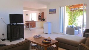 A living room with a television, a coffee table, and a sofa. There is a kitchen area in the background with a refrigerator and a dining table. - Quiet family friendly vacation home for 6 to 10 pers. (Cabrieres d' Avignon)