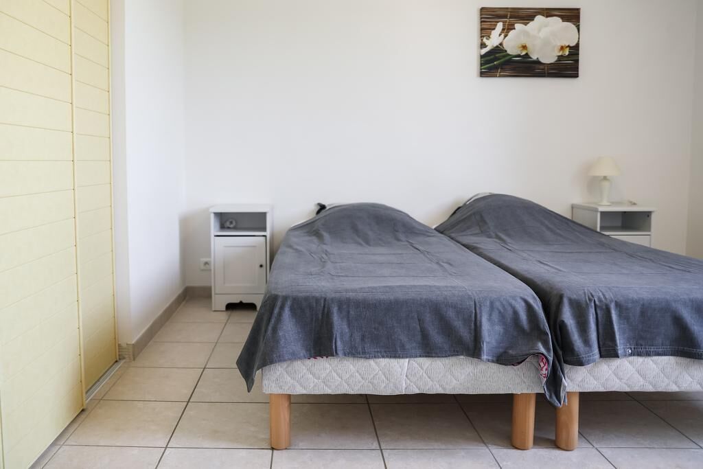 A small, clean room with two single beds, a nightstand with a lamp, and a wall-mounted picture of flowers.
