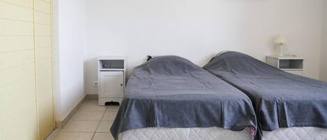 A small, clean room with two single beds, a nightstand with a lamp, and a wall-mounted picture of flowers.