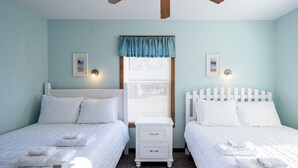 Ein Zimmer mit zwei Betten, einem Nachttisch und einem Deckenventilator.
