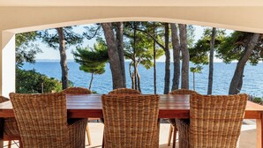 Een eetruimte met uitzicht op zee, met rieten stoelen en een houten tafel.