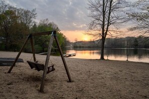 A wooden swing set on a sandy beach with a lake and trees in the background. - Goshorn Lake Resort Cottage #23 (Saugatuck)