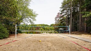 Una cancha de voleibol de playa con arena, una red, rodeada de árboles y un lago.