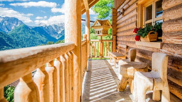 A wooden log cabin with a balcony overlooking a mountainous landscape.