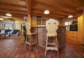 A rustic cabin interior with a stone wall bar area, wooden furniture, and a cozy seating area.