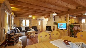 A cozy log cabin interior with a fireplace, wooden furniture, and a television.