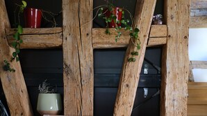 Eine rustikale Holzbank mit zwei Kissen, eine Holzleiter und Kübelpflanzen vor einer dunklen Wand.