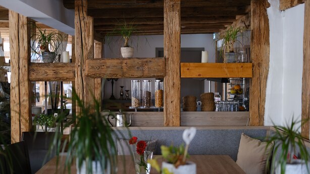 Ein Holzespeisetisch mit Blumentöpfen, einer Glasvase mit Blumen und einer grau gepolsterten Bank.