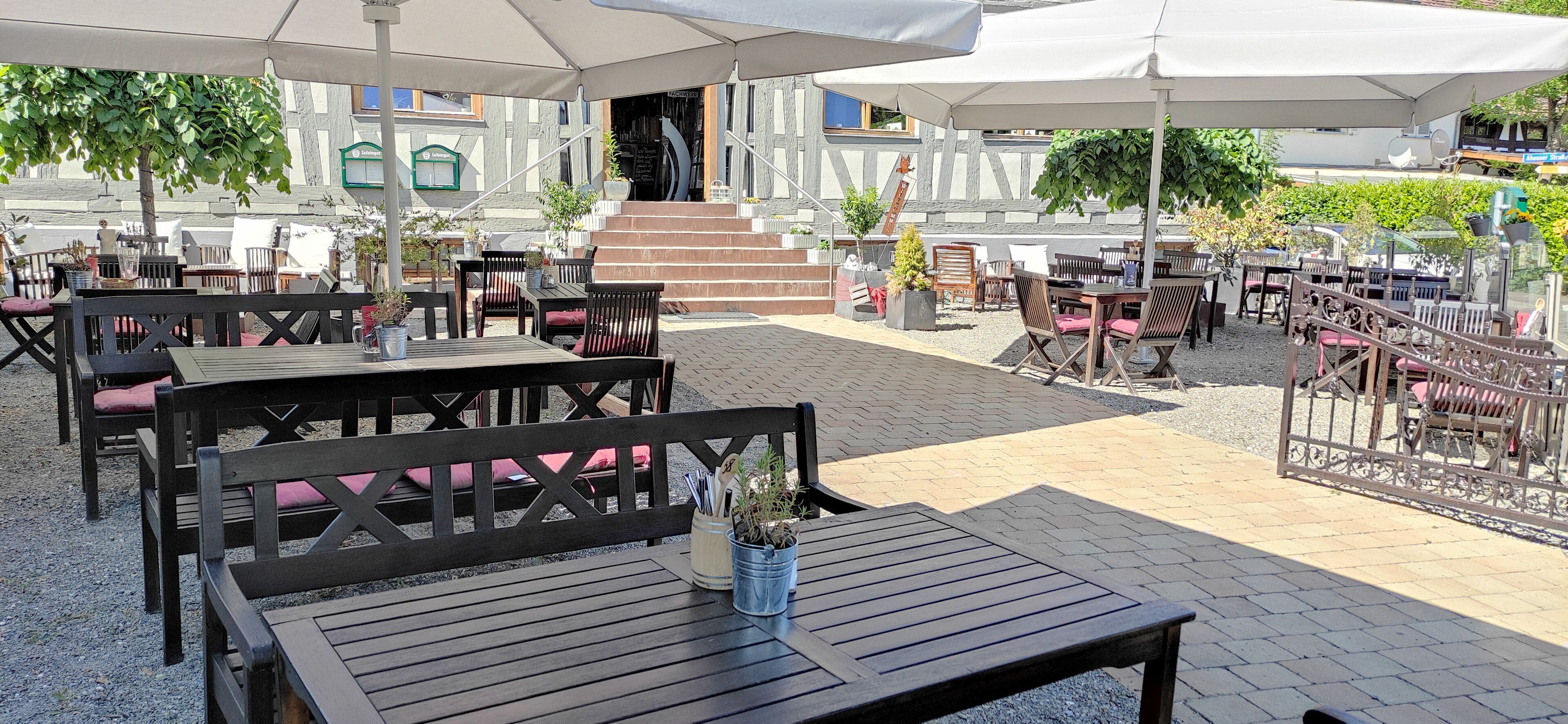 An outdoor patio area with wooden tables and chairs, umbrellas, and potted plants.