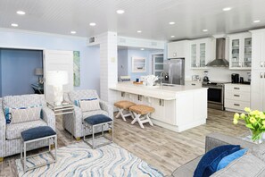 A modern kitchen with white cabinetry, a central island, and a dining area with wicker furniture. - Luxury 3BR Condo at Silver Shells w/ Beach Service! (Destin)