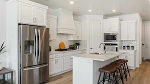 A modern kitchen with white cabinetry, stainless steel appliances, a central island with stools, and a microwave above the sink. - Cloud 9 At Desert Color: Desert Color Lagoon + Beaches (St. George)