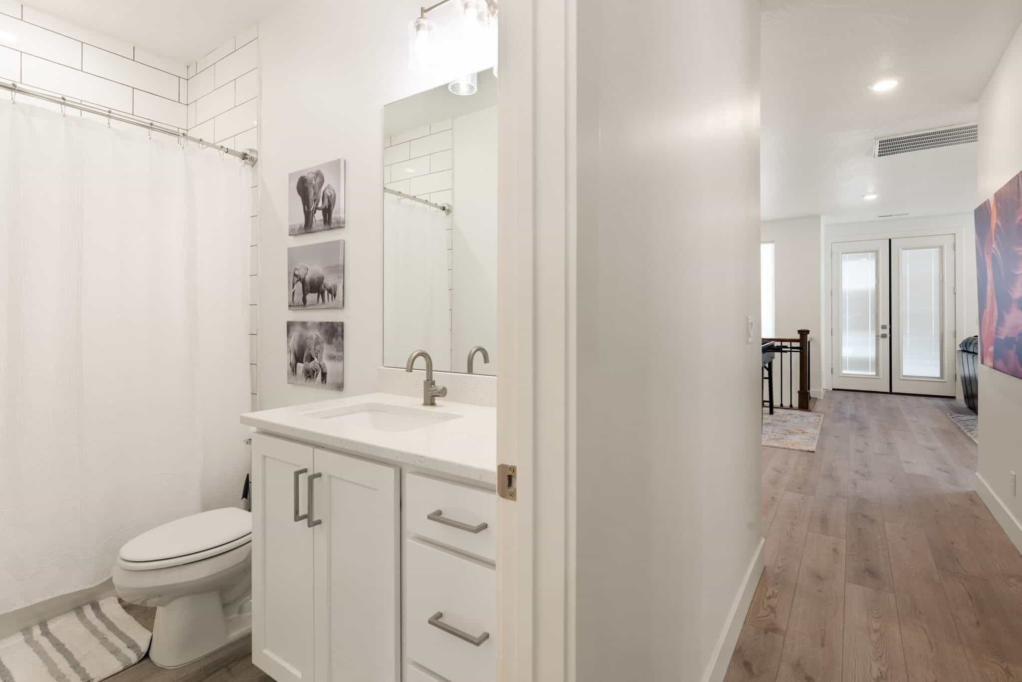Un baño moderno con inodoro, lavamanos y espejo. Hay cuadros enmarcados en la pared.