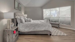 A bedroom with a bed, bedside table, lamp, and window with blinds. - Frisco Spacious & Cozy Bling Home by Aya (Frisco)