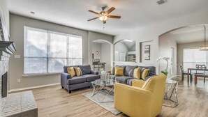 A spacious living room with a gray sofa, a yellow armchair, and a coffee table. There is a ceiling fan and a fireplace. - Frisco Spacious & Cozy Bling Home by Aya (Frisco)