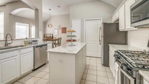 A modern kitchen with white cabinetry, a central island, a stainless steel refrigerator, and a built-in oven. - Frisco Spacious & Cozy Bling Home by Aya (Frisco)