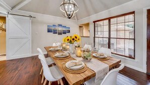 A dining area with a wooden table set for six, white chairs, and a chandelier. - Stunning Gables House, Basketball Court (Dallas)