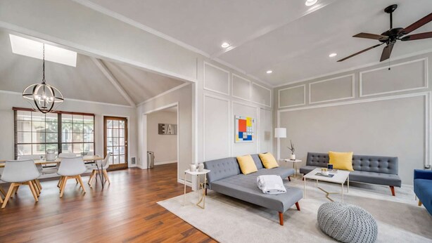 A spacious living room with a grey sofa, a coffee table, and a dining area with wooden chairs and a chandelier. - Stunning Gables House, Basketball Court (Dallas)