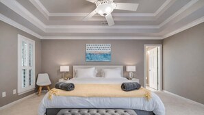 A bedroom with a large bed, two bedside tables with lamps, a ceiling fan, a window with shutters, and a door. - Stunning Gables House, Basketball Court (Dallas)
