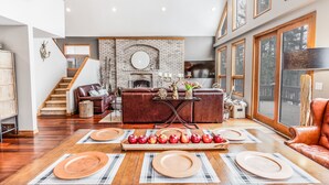 A spacious living area with a fireplace, a dining table set with plates and apples, and a leather sofa. - Quaint + Modern Lakeview Home on Sacandaga Lake (Hadley)