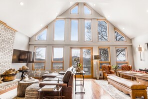 A spacious living room with a high ceiling, large windows, a fireplace, and a dining area.