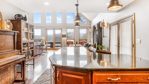 A spacious kitchen with a large island, wooden cabinetry, and pendant lighting. - Quaint + Modern Lakeview Home on Sacandaga Lake (Hadley)