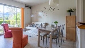 Un salon moderne comprenant un coin repas, un canapé, un fauteuil rouge, un meuble en bois et un mur décoré d’autocollants représentant des oiseaux.