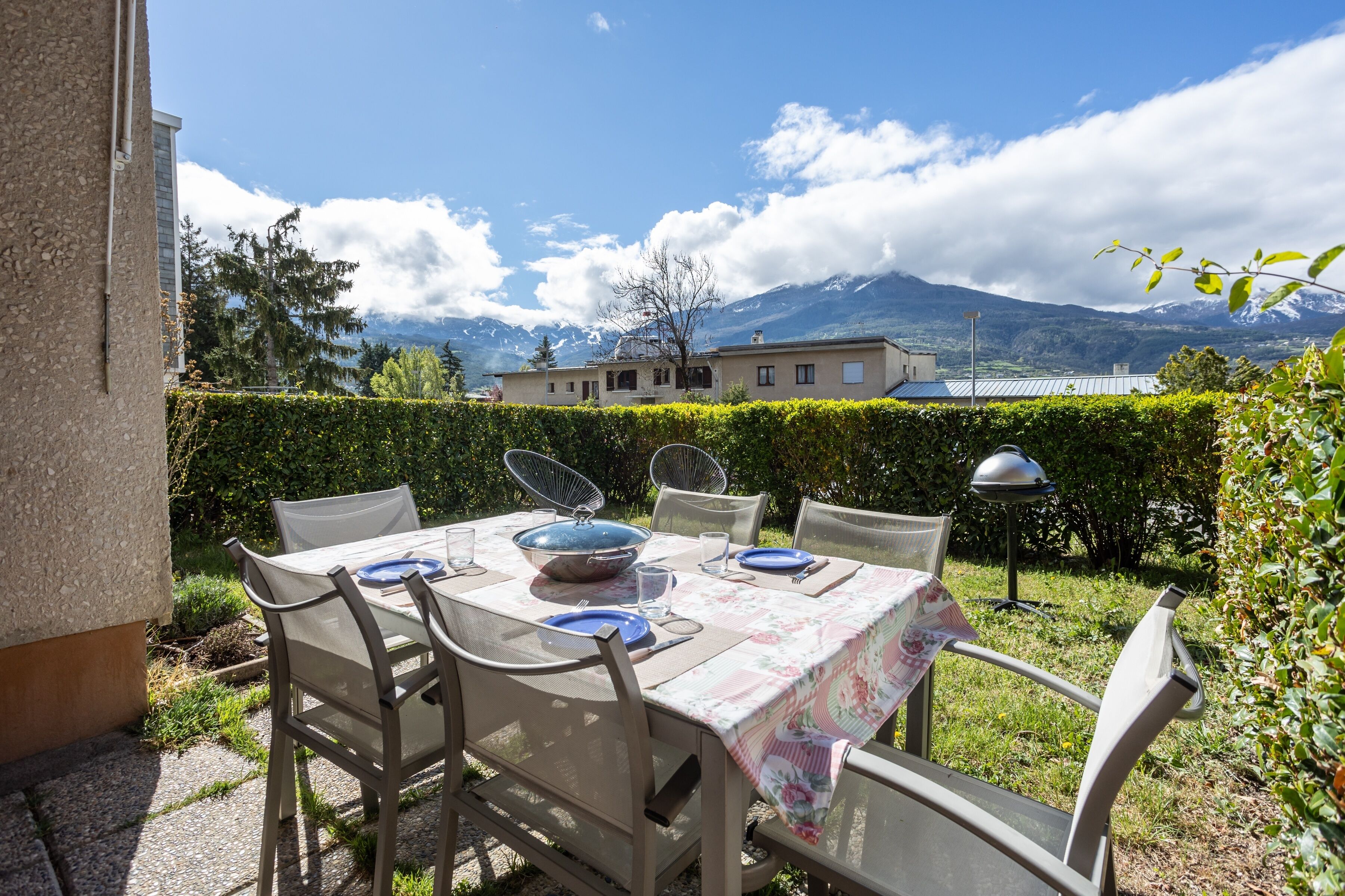 An outdoor dining area with a table set for four, chairs, and a view of mountains in the background.