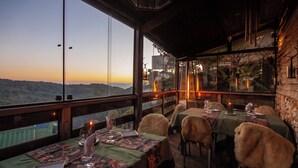 Een restaurant met gedekte tafels, grote ramen met uitzicht op het landschap en een gezellig interieur met houten balken en rustieke decoratie.