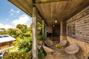 Eine überdachte Terrasse mit Steinboden, Korbstühlen und einem kleinen Tisch mit Blumen.
