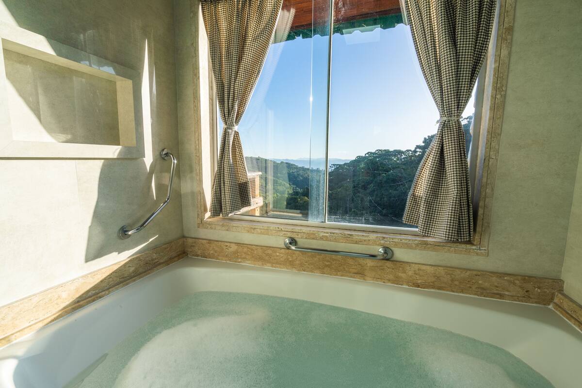 Ein Badezimmer mit Badewanne, einem Fenster mit Vorhängen und einer Handstange.