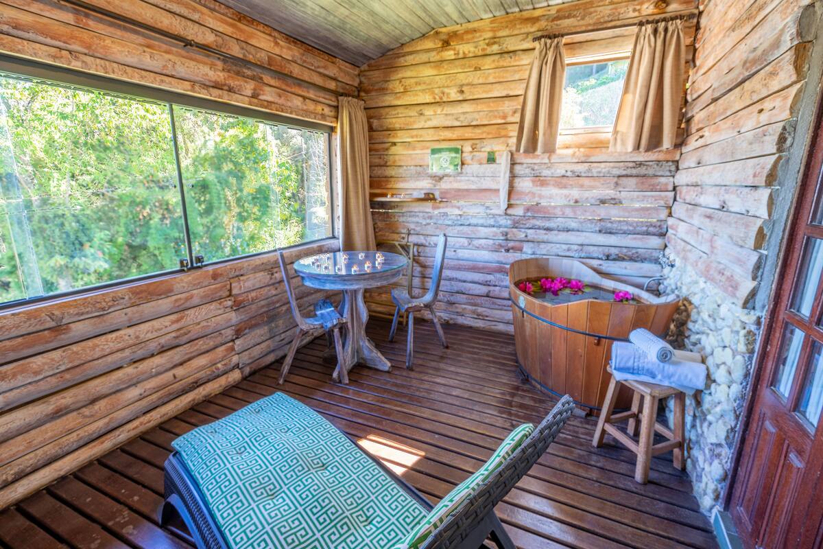 Eine Holzhütte mit einem runden Tisch, Stühlen, einer Bank und einer Holzwanne.