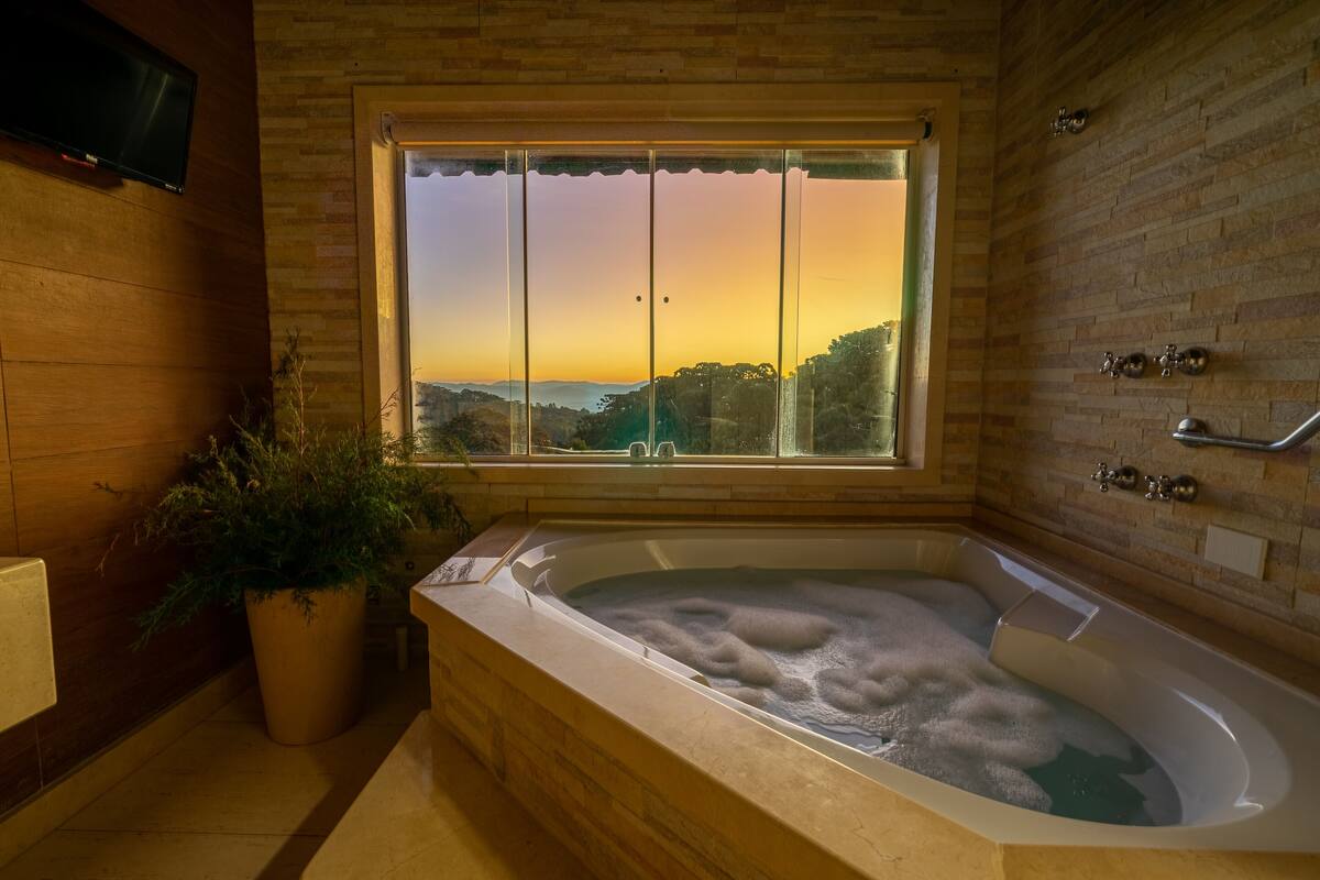 Ein Badezimmer mit einer großen Badewanne, einer Topfpflanze und einem Fenster mit Blick auf den Sonnenuntergang.