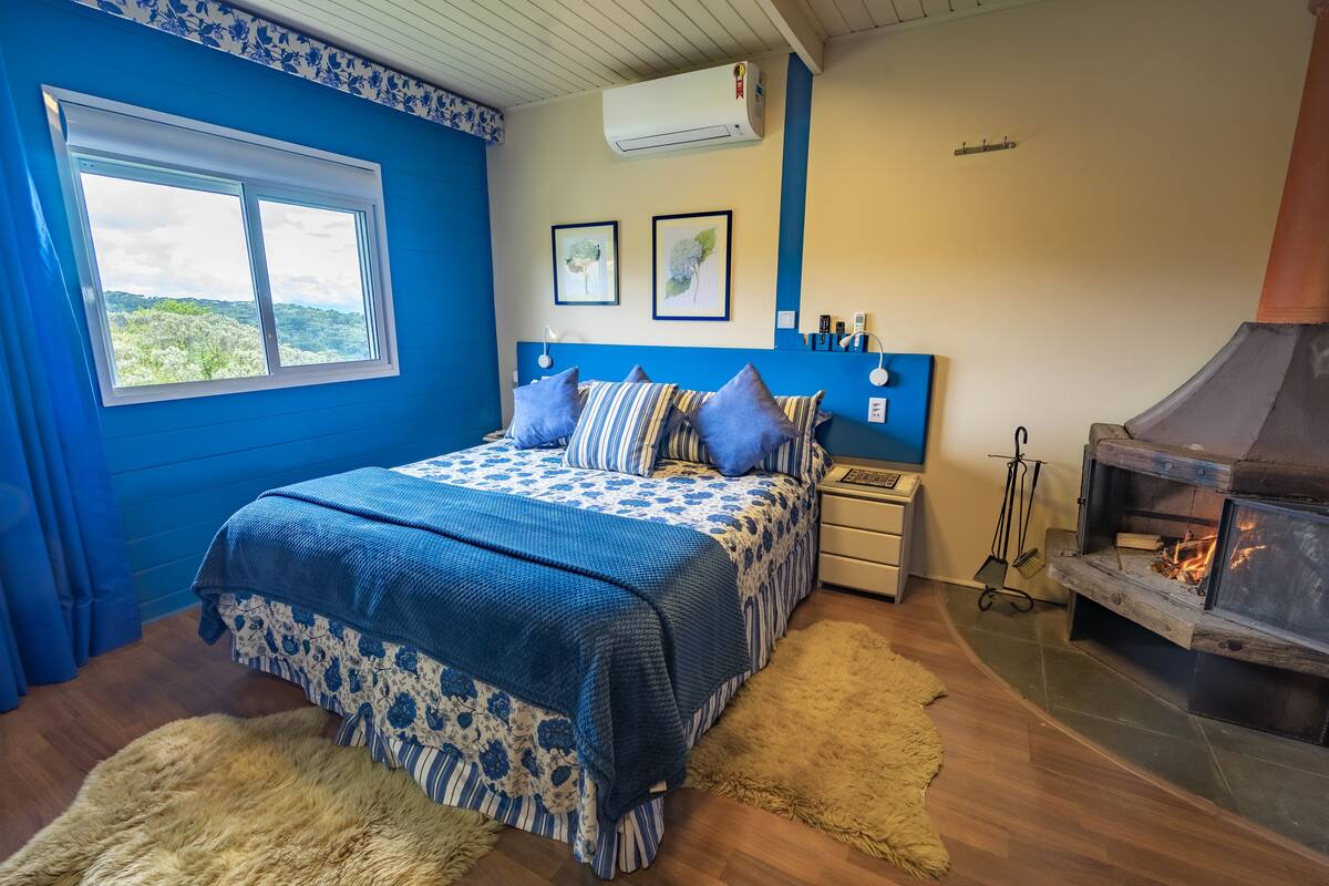 Ein Schlafzimmer mit einem Bett, einem Kamin, einem Fenster mit Aussicht und einer Wand-Klimaanlage.