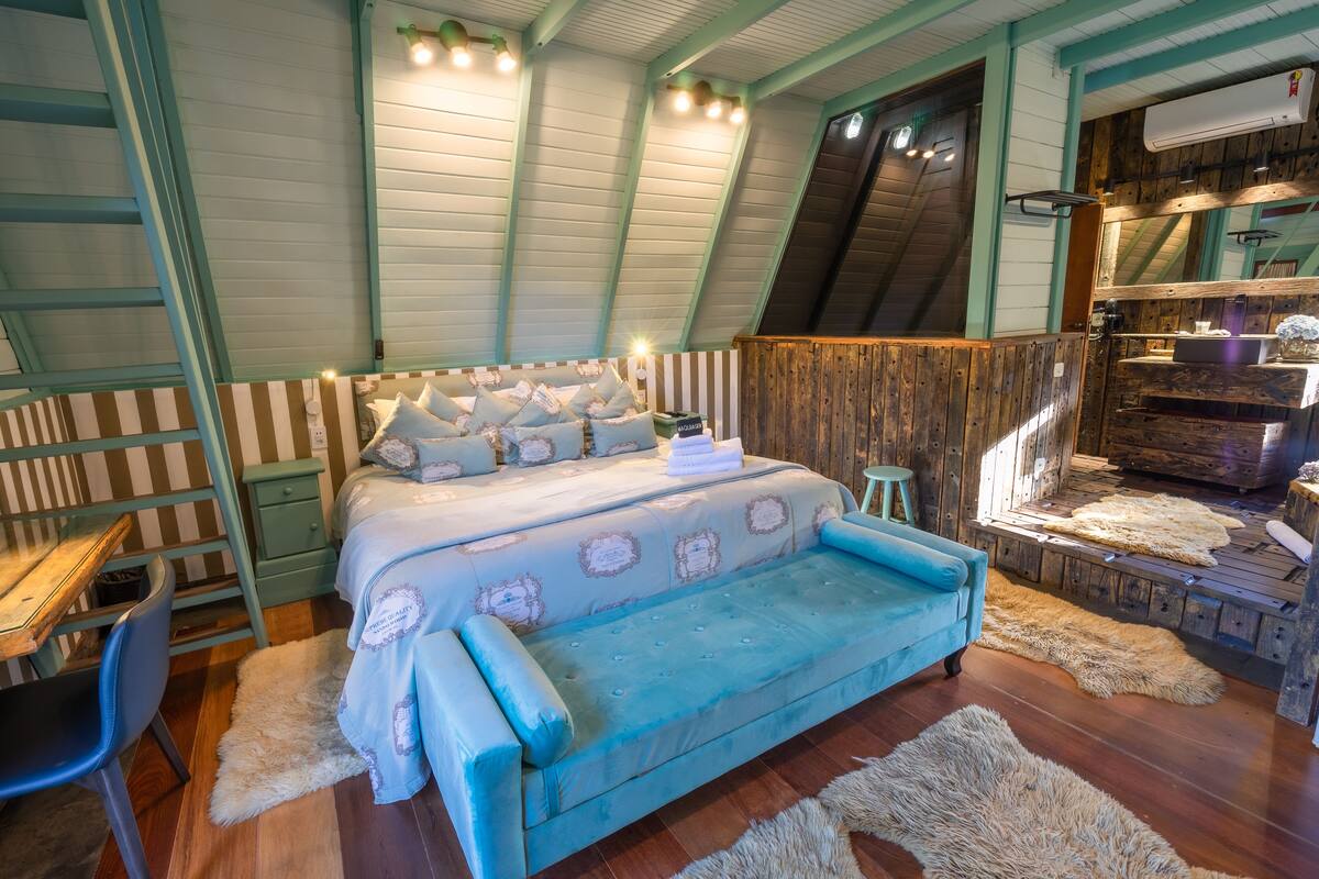 Ein gemütliches Schlafzimmer im Dachgeschoss mit einem Bett, einem blauen Sofa, Holzwänden und einer rustikalen Treppe.