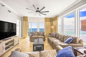 Ein geräumiges Wohnzimmer mit großem Flachbildfernseher, Ledersofas, einem Couchtisch und Deckenventilator.