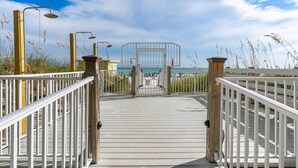 A wooden boardwalk leading to a beach area with a clear view of the ocean and a distant building. - Jade East Towers~Beach Front w/Amazing Unparalleled  Sunrise and Sunset Views (Jade East Towers , Destin)