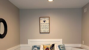 A bedroom with a bed featuring a blue and white quilt, a wall-mounted decorative sign, and a white headboard. - Beach block Wildwood Crest ground level condo-103 (Wildwood Crest)