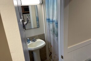Un baño con lavamanos blanco, espejo y cortina de ducha con estampado de olas.