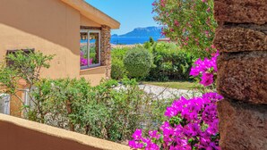 Un edificio in stile mediterraneo con facciata in pietra, un balcone con ringhiera in pietra e vista sul mare e sulle montagne sullo sfondo.