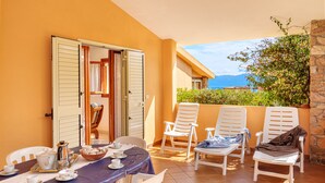 Un balcone con tavolo apparecchiato per la colazione, sedie bianche e vista sul mare.